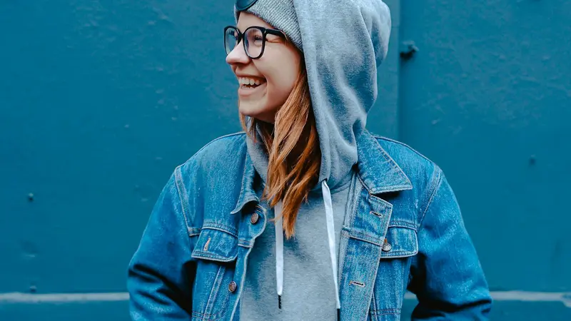 Smiling young person in a denim jacket against a bright blue wall