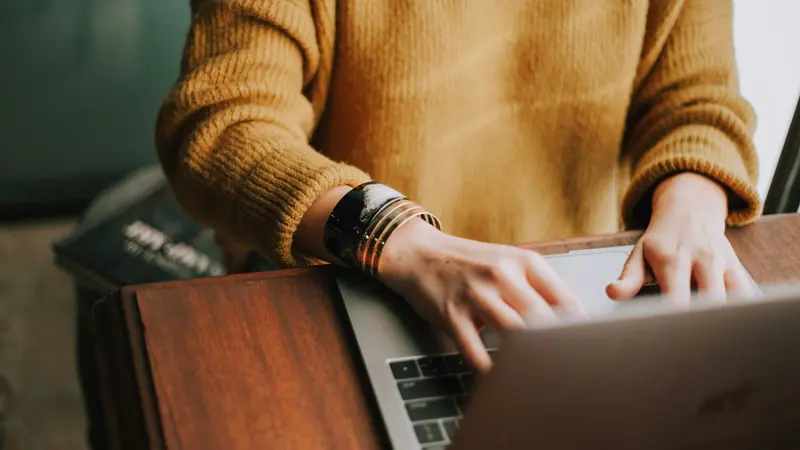 Person in a cozy yellow sweater working calmly on a laptop