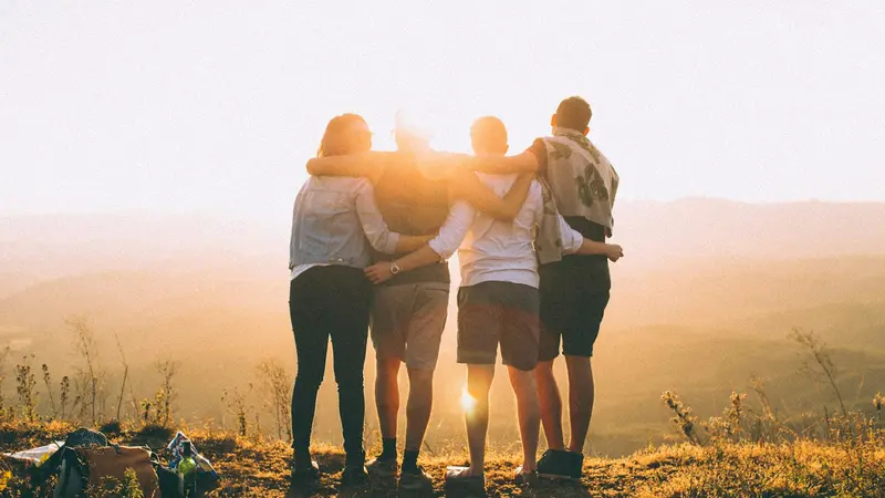 Group of friends with arms around each other watching a sunset together